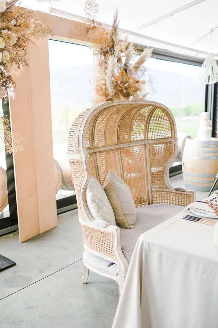 Peacock rattan chair with white cushions decorated with dried floral arrangements in a bright venue.