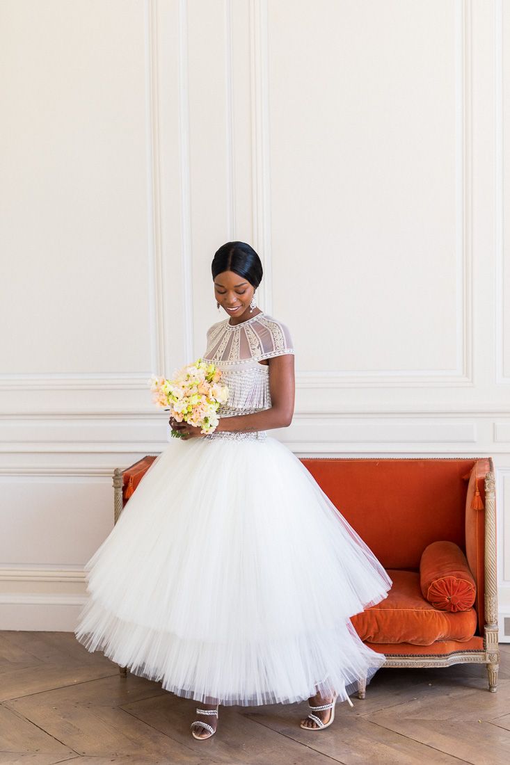 Elegant tea-length tulle wedding dress with delicate lace details and pastel bouquet.