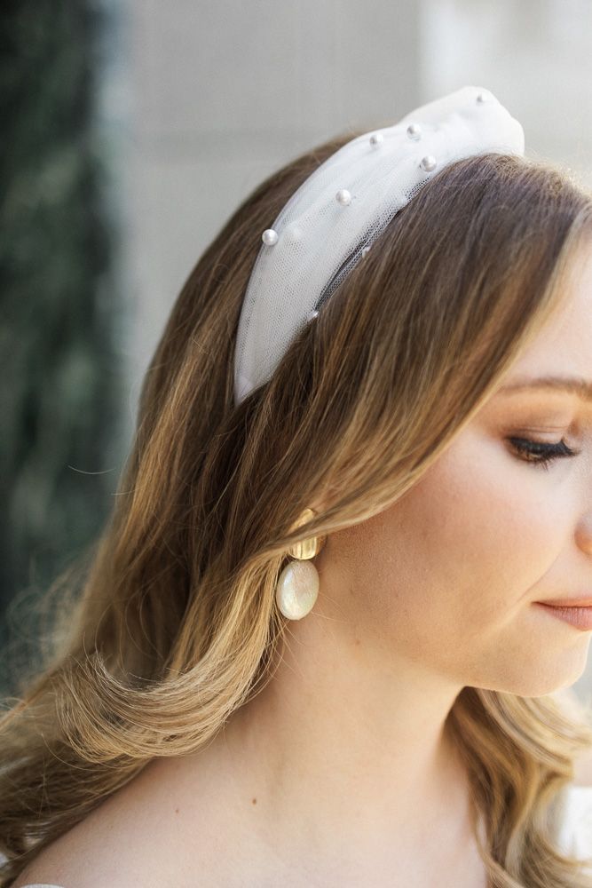 Close-up of a white pearl-studded headband accessorizing wavy blonde hair with pearl drop earrings.