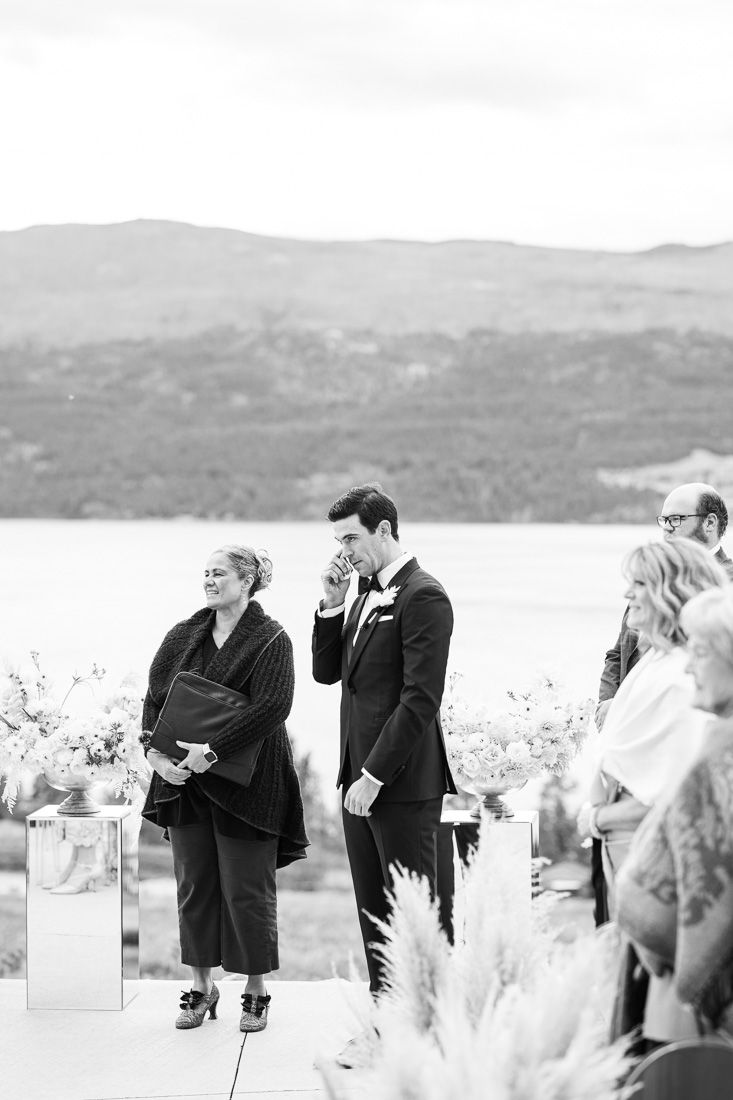 Black and white photo of wedding ceremony guests gathered against mountainous backdrop.