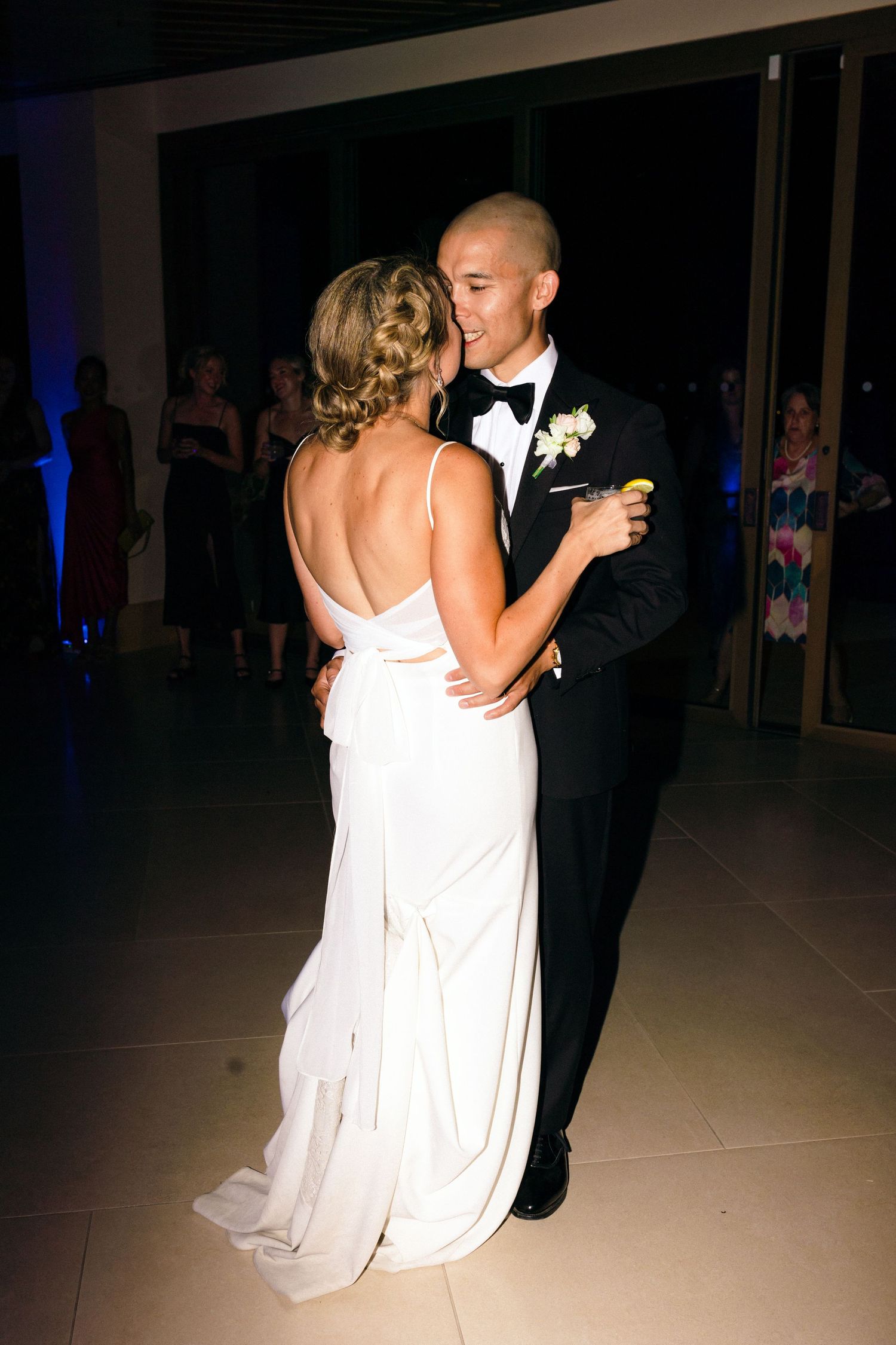 Couple sharing their first dance in formal attire under dramatic lighting.