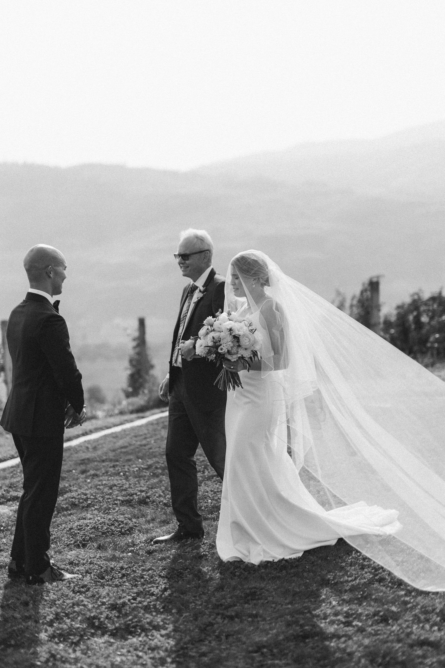 Wedding couple sharing an intimate moment on a hillside with flowing veil in black and white.