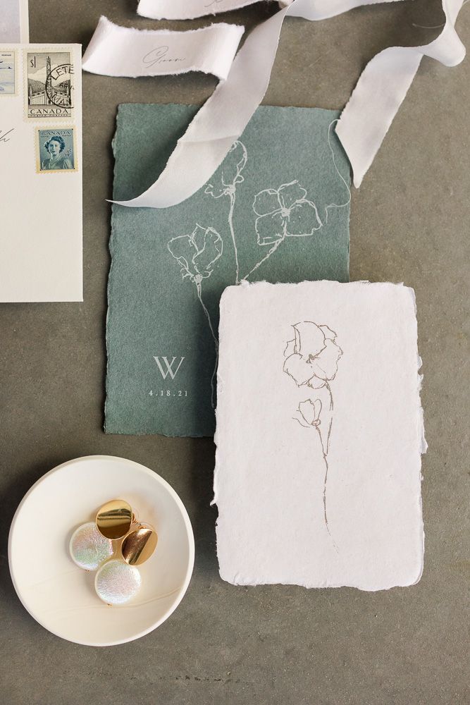 Elegant wedding stationery with delicate floral sketches on sage green paper and white ribbons.
