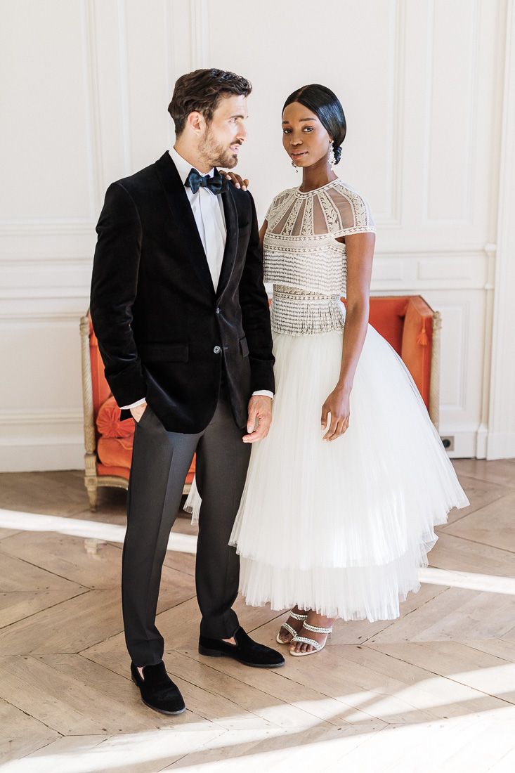 Elegant couple in formal attire, with groom in black tuxedo and bride wearing white beaded gown with tulle skirt.