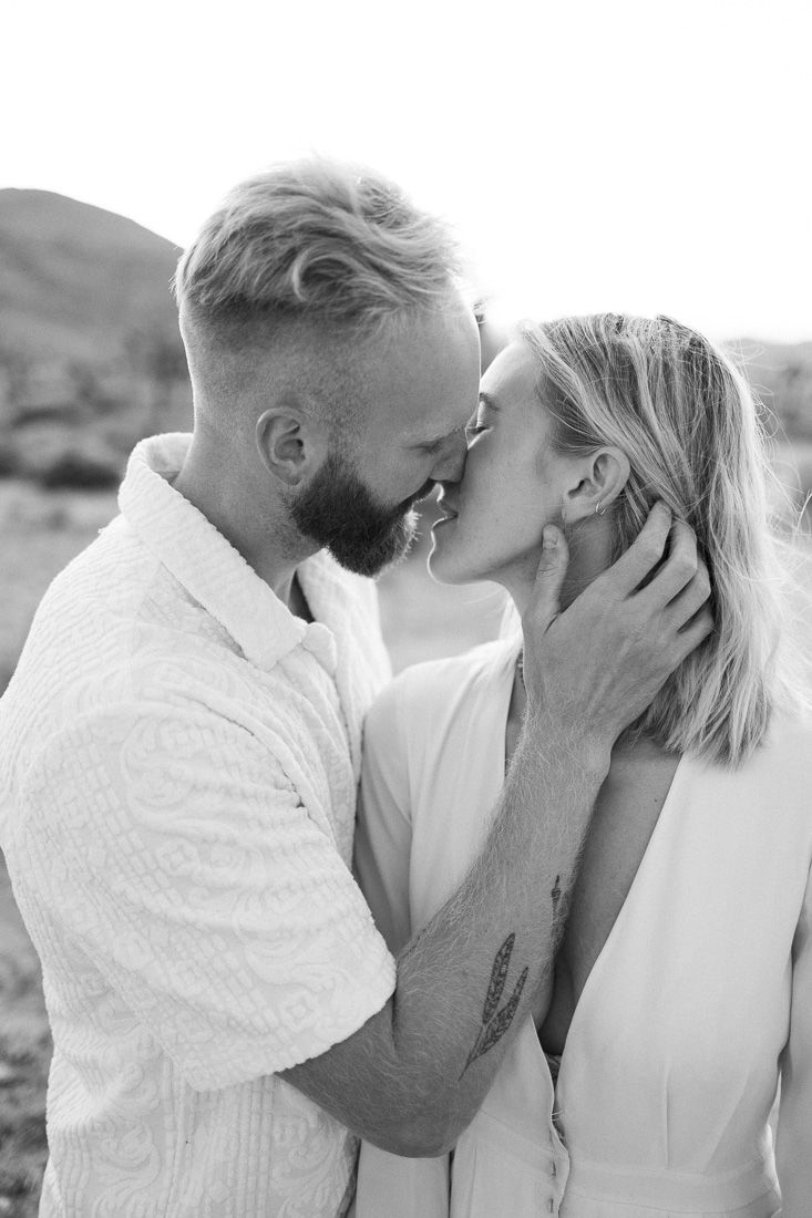 A black and white portrait of a couple sharing an intimate moment outdoors.