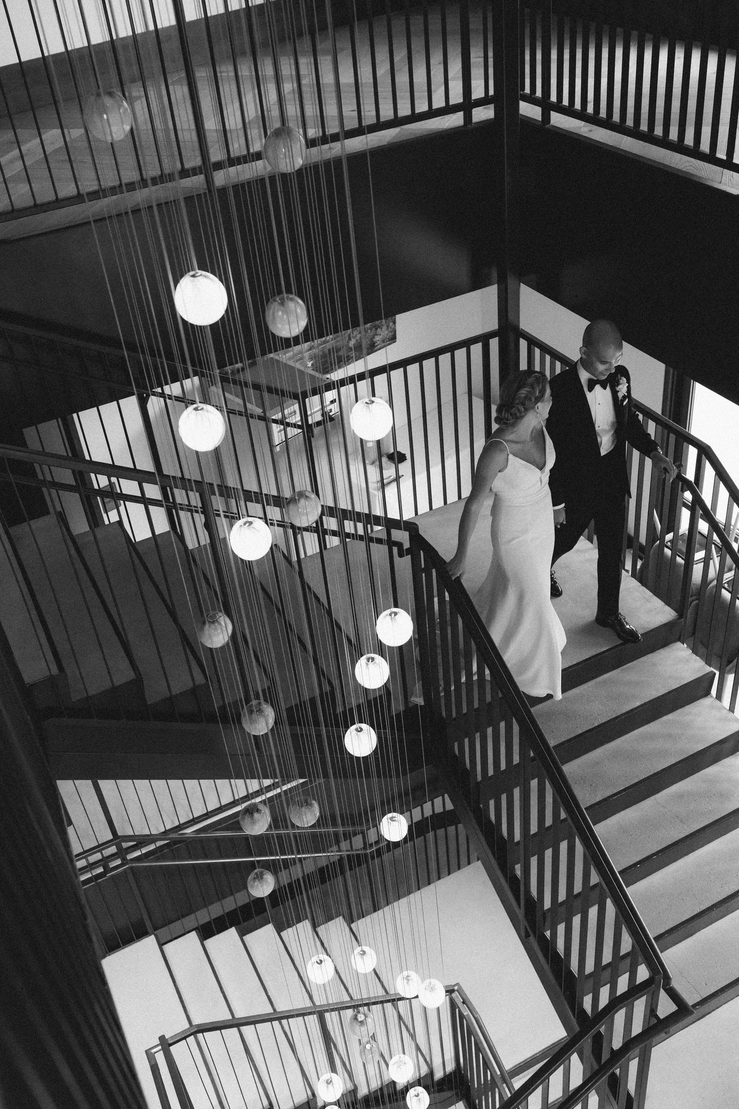 Artistic black and white photo capturing a staircase with modern pendant lighting and wedding dress details.