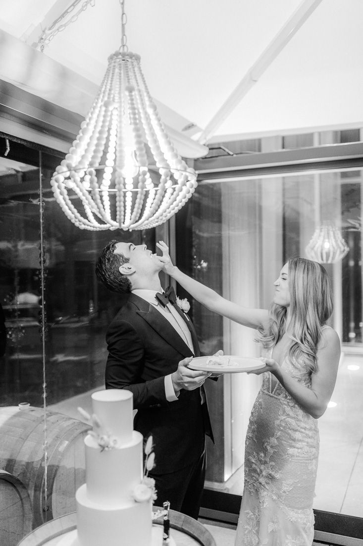 A playful cake-feeding moment between newlyweds under an elegant crystal chandelier.