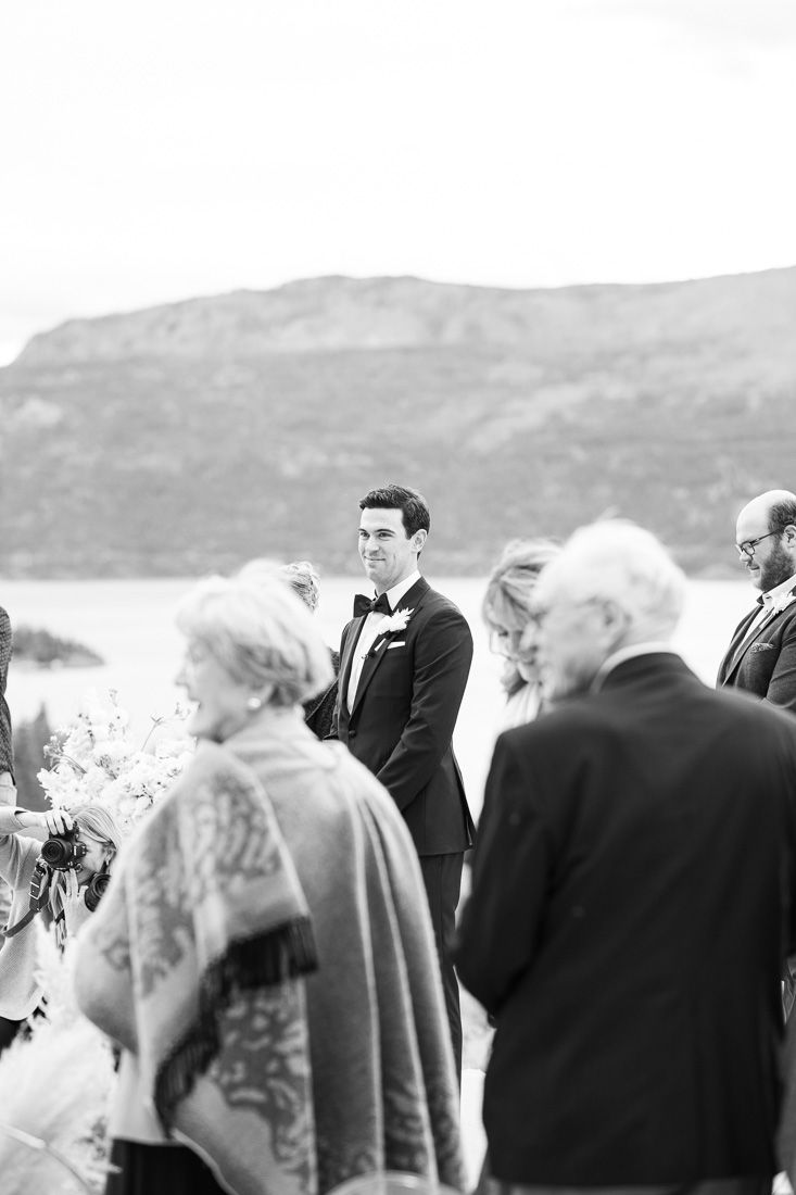 Outdoor mountain wedding ceremony gathering with lake and hills in background.
