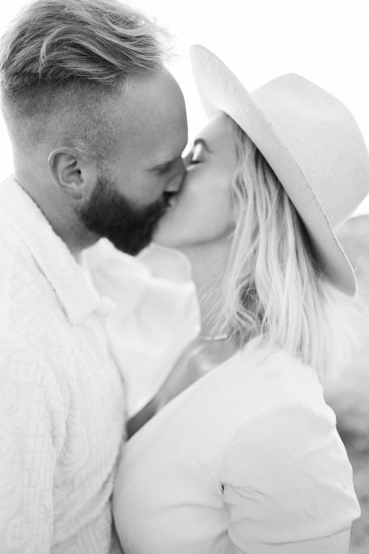 Black and white intimate portrait of a couple in white clothing sharing a kiss.