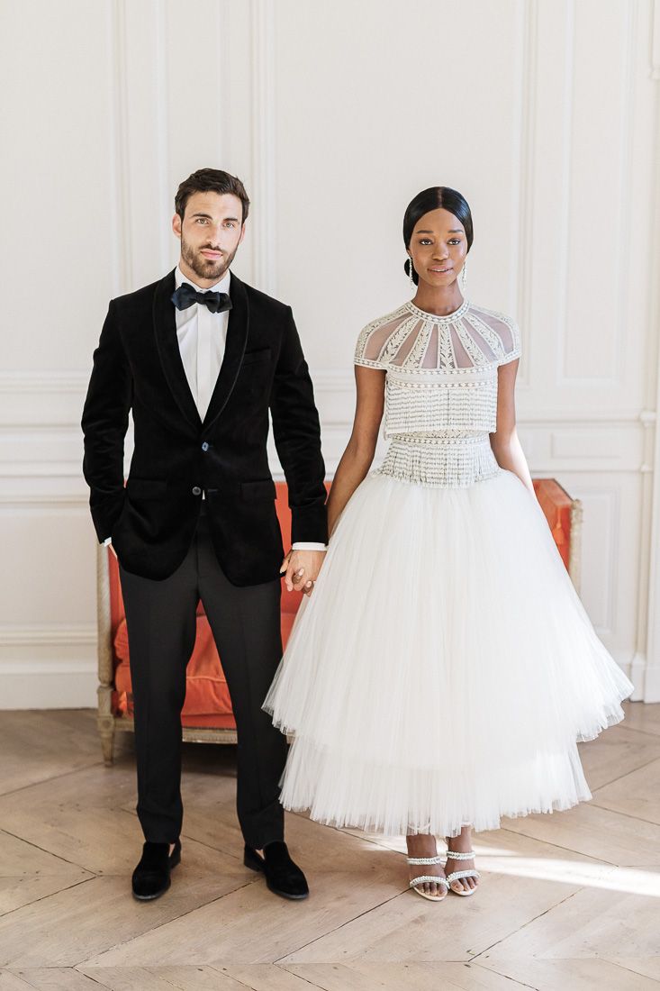 Wedding couple in formal attire standing together against white paneled walls.