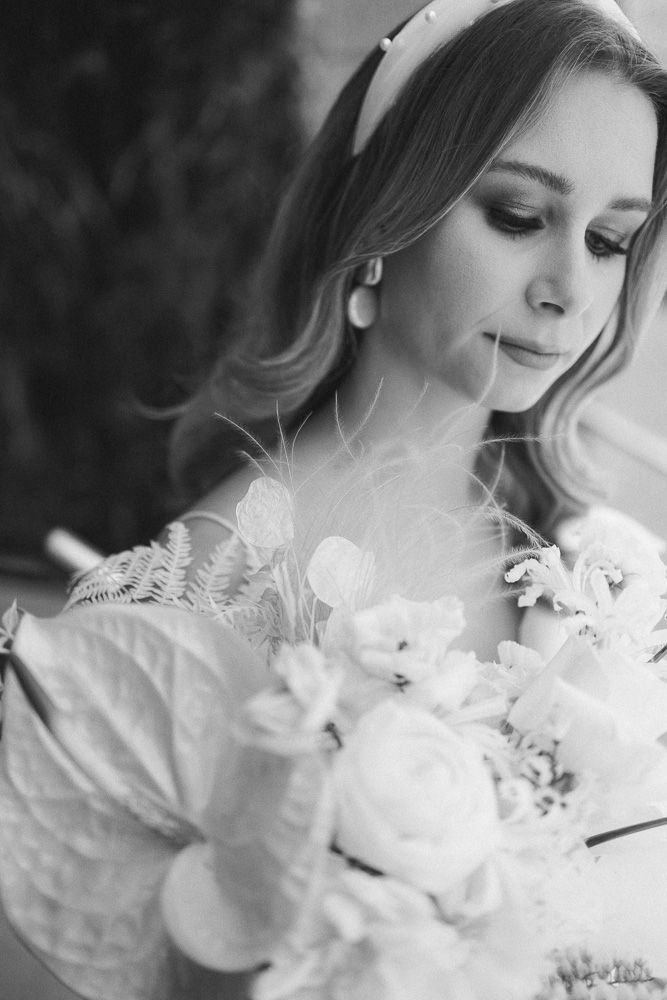 Black and white portrait of a bride holding a soft white bouquet with feather accents.