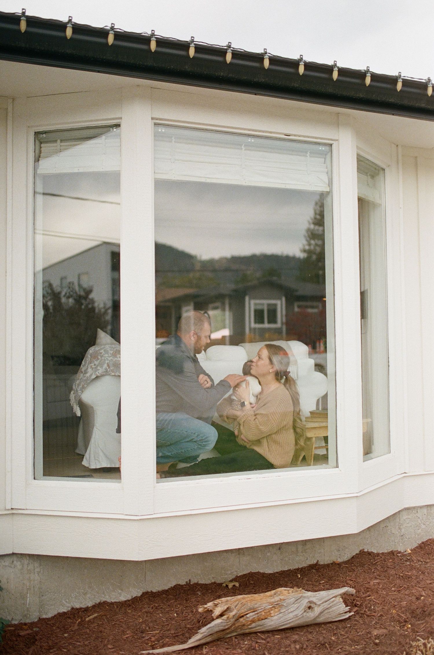 People relaxing by a bay window in a cozy home interior with white trim and natural lighting.