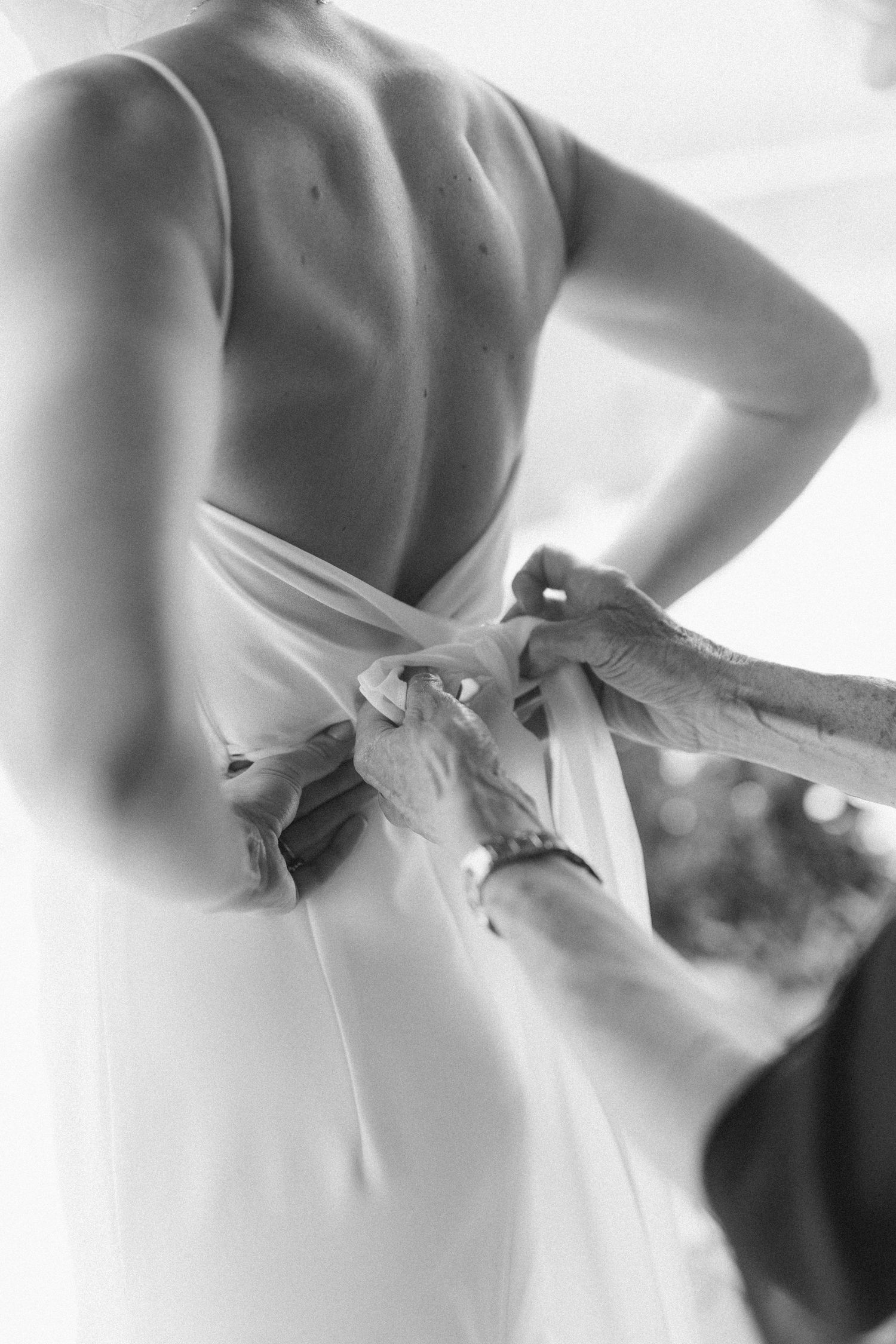 Black and white sequence of a bride's dress being laced up in elegant detail.