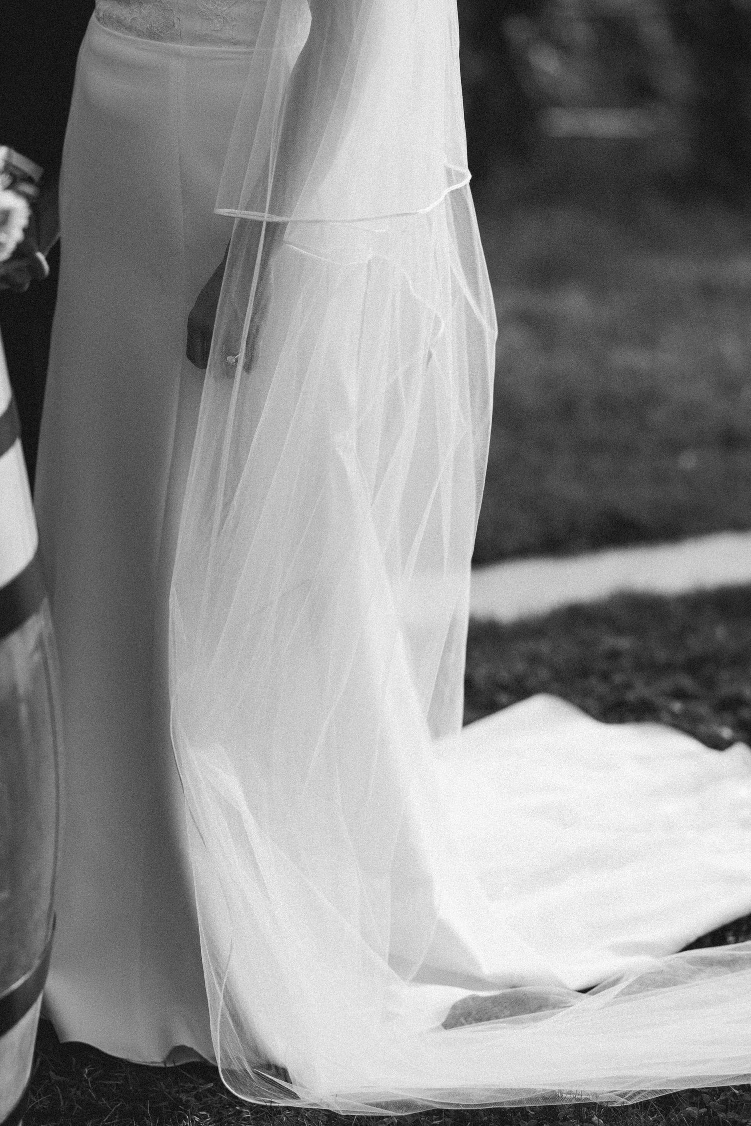 Detail shot of flowing white wedding dress and veil against dark ground.