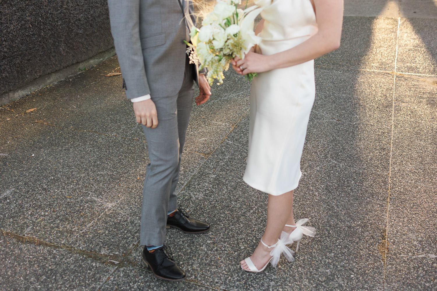 Close-up of formal attire showing grey suit next to white dress with bouquet.