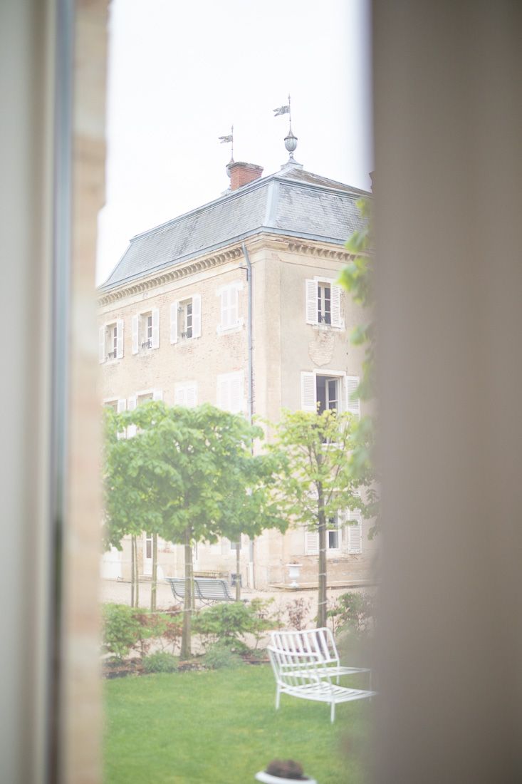 Garden view of French manor house through window frame with white bench in foreground.