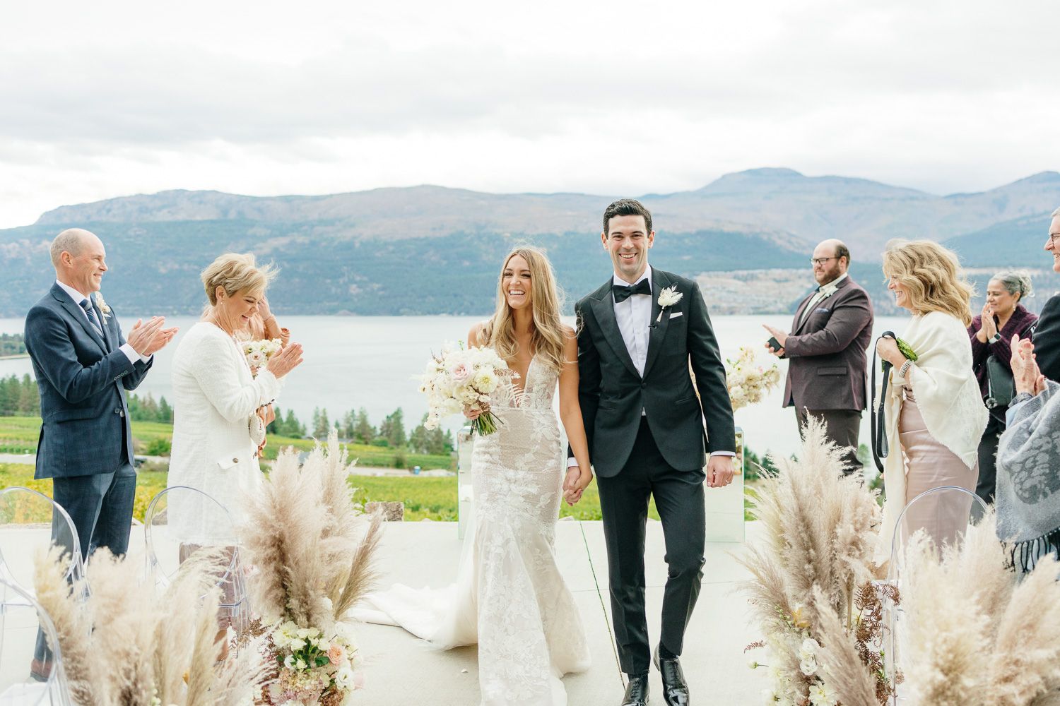 Wedding party and guests celebrate on an outdoor terrace with mountain scenery.