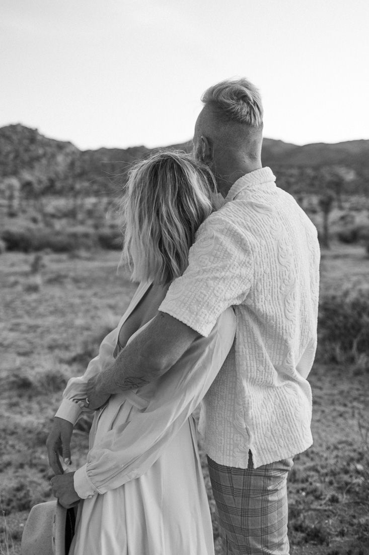 Black and white photo of a couple embracing in a desert landscape.