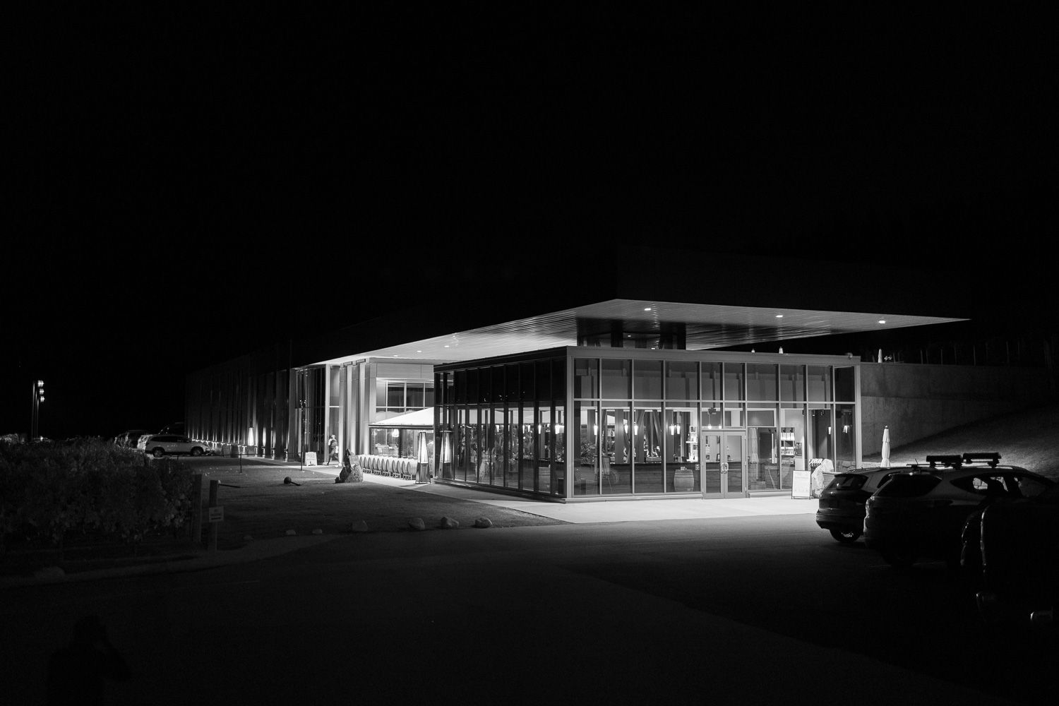 A black and white nighttime exterior view of a modern glass building with illuminated windows.