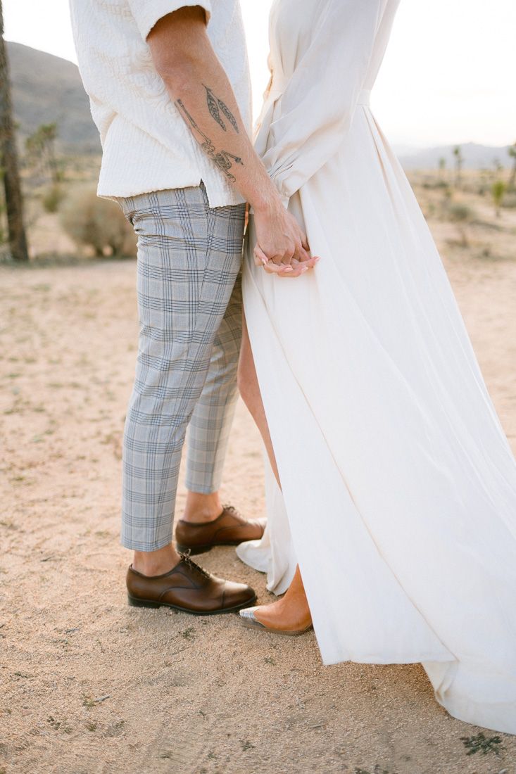 Detail shot of couple's coordinated outfits and footwear against desert sand.