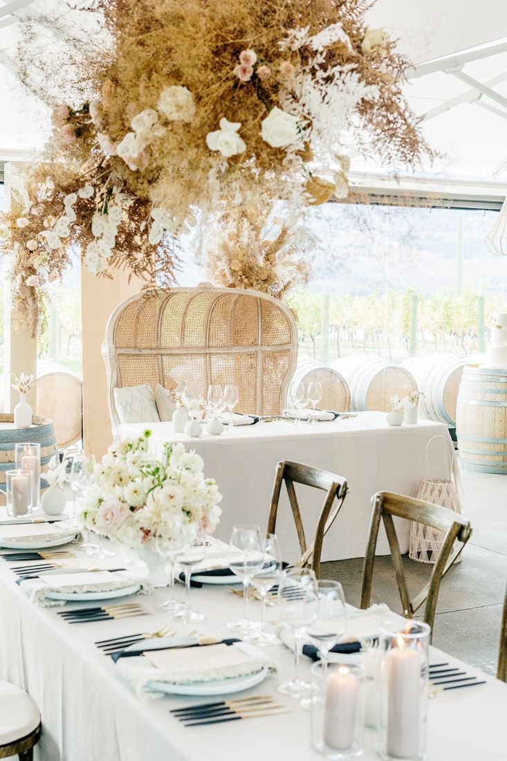 Wedding reception table with dramatic dried floral ceiling installation and rattan peacock chairs.