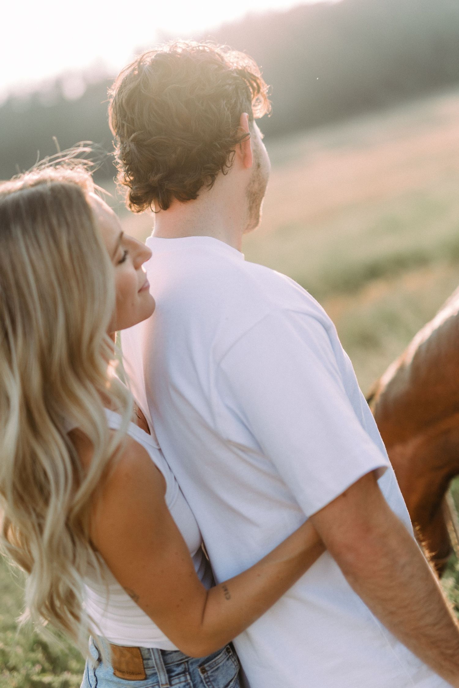 Intimate moment captured between a couple and their horse in a sunlit field.