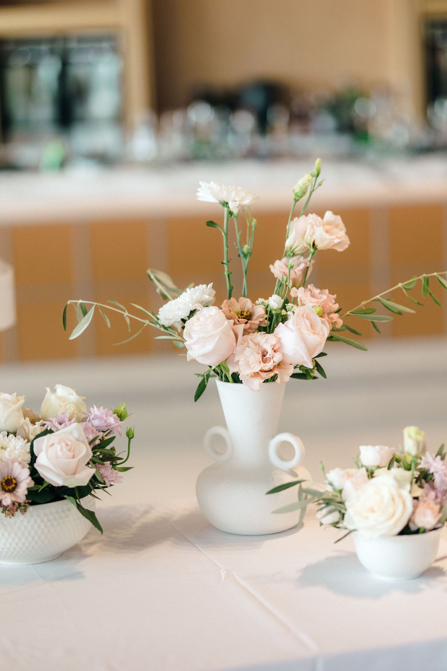 Delicate floral centerpieces featuring pink roses arranged in white teacups on a table.