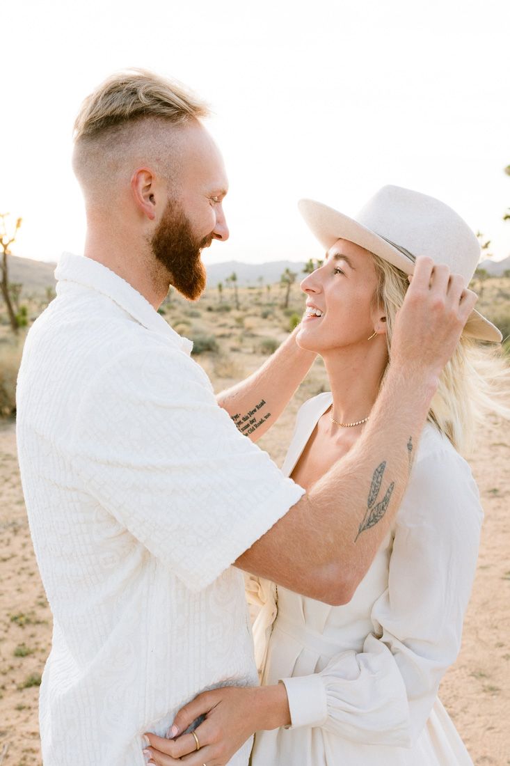 Sun-drenched desert portrait of couple in white with woman wearing stylish hat.