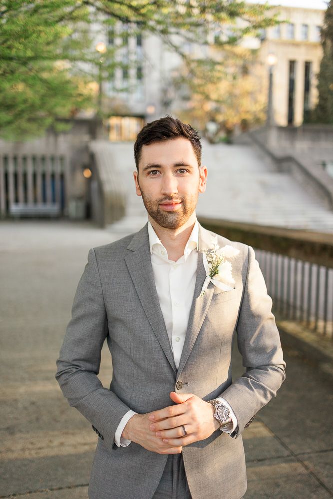 A formal portrait of someone wearing a gray suit with boutonniere against an architectural backdrop.