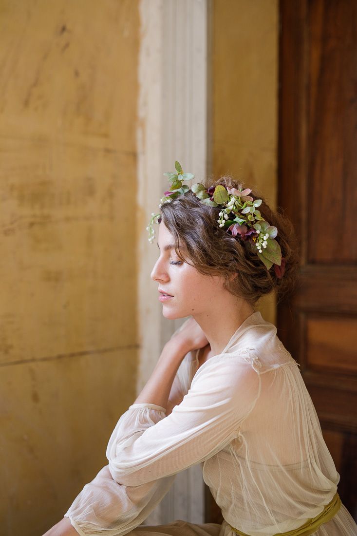 Side profile portrait showing romantic styling with floral crown against wooden door backdrop.