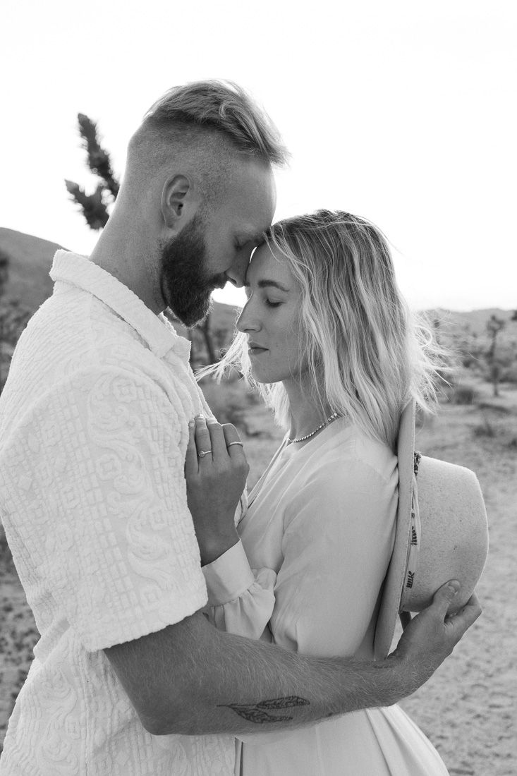 Black and white portrait of couple sharing intimate moment in desert landscape.