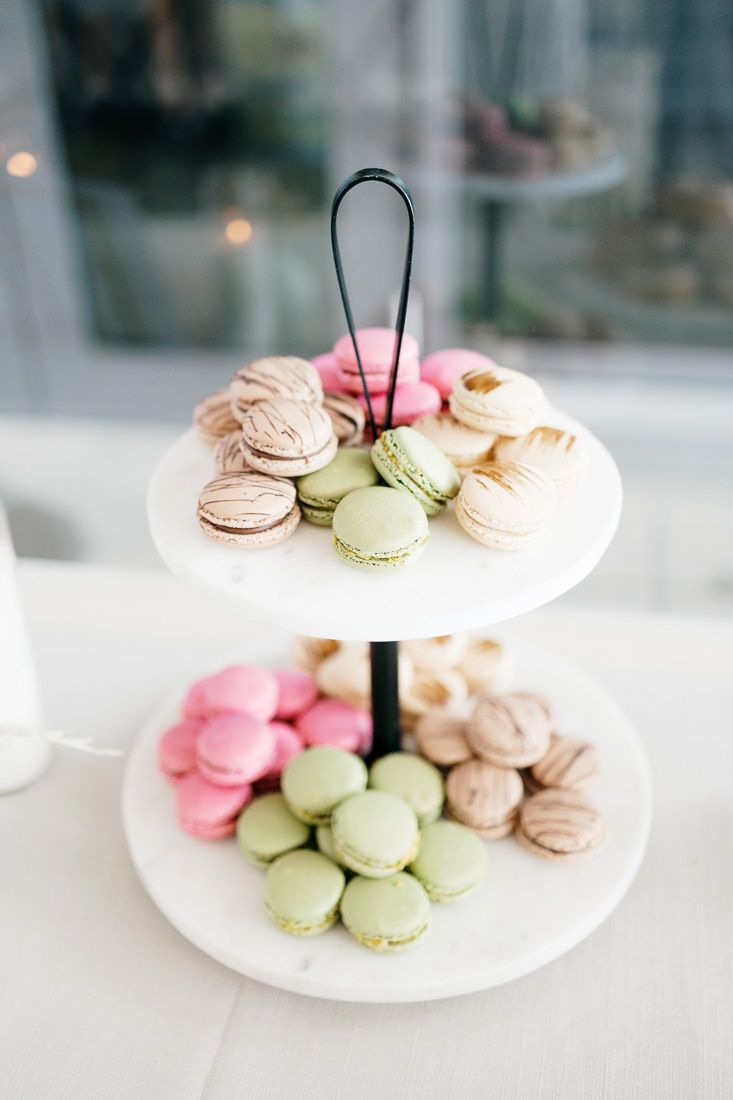 Two-tiered dessert stand displaying colorful macarons in pink, green and beige shades.