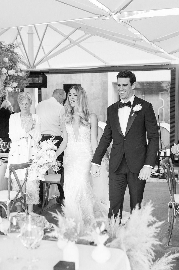 A wedding celebration under a white tent with elegant table settings and pampas grass decor.