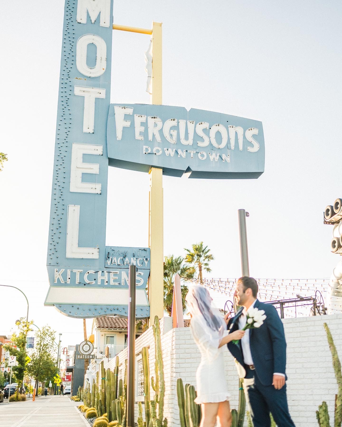 Vintage motel and Ferguson's restaurant sign with palm trees against a bright sky in an urban setting.