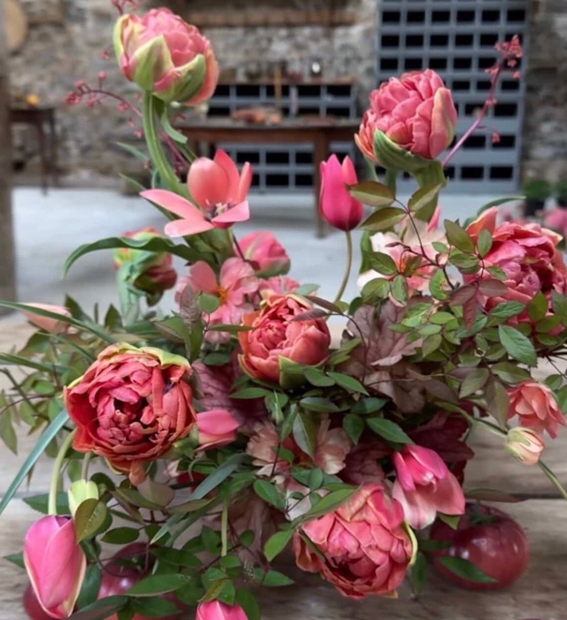 A collection of pink garden roses arranged in a rustic display with green foliage and vintage decor elements.
