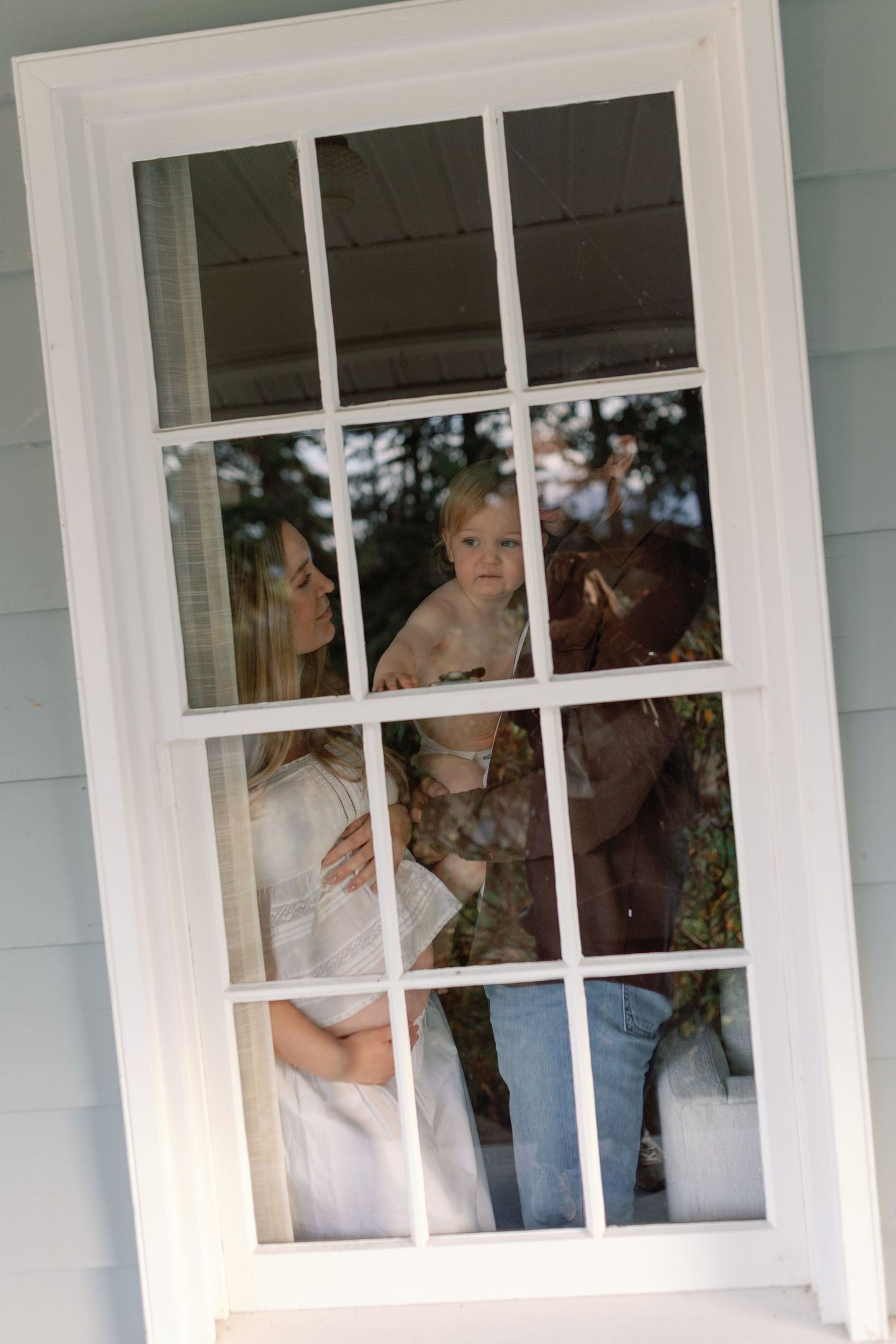 A view through a white-framed window pane showing figures standing behind the glass in a domestic setting.