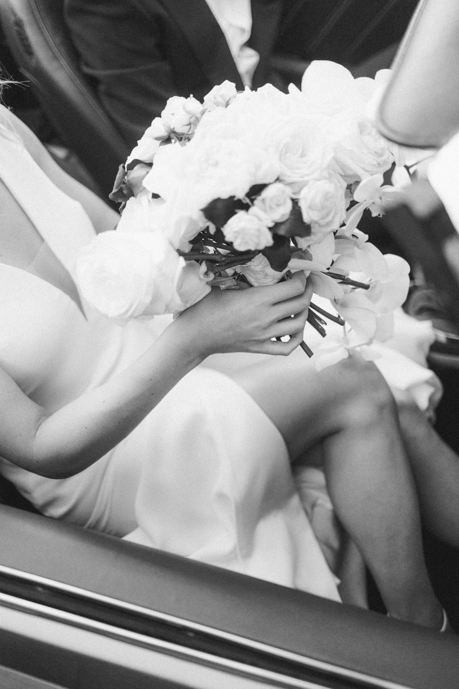 Black and white photo of bridal bouquet with white roses resting on white dress fabric.