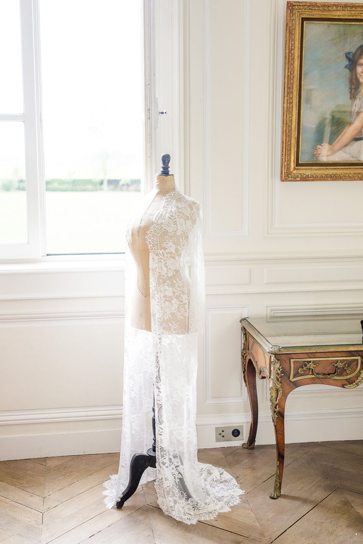 Delicate lace wedding dress on mannequin form in elegant white room.