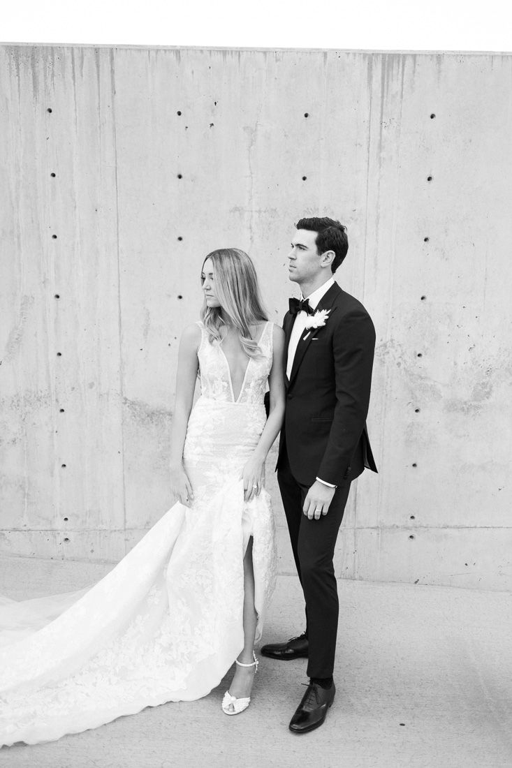 Black and white portrait of couple in wedding attire against concrete wall.