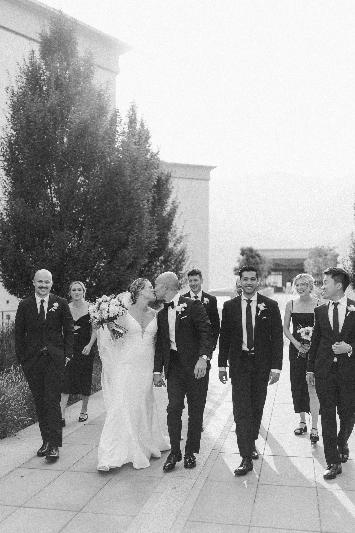 Wedding party walking in formal attire outside a modern building.