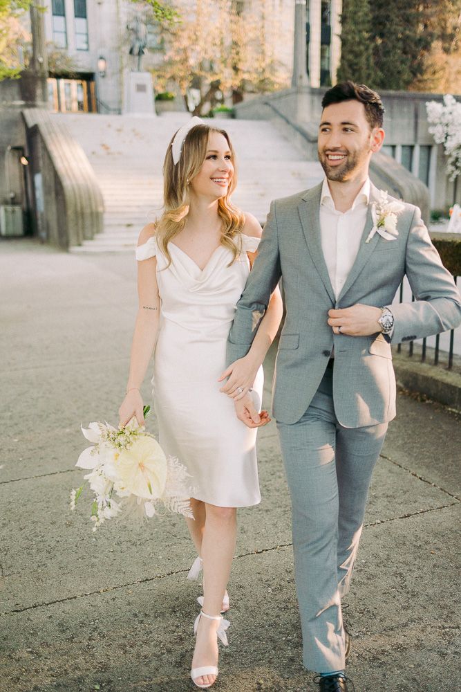 Couple in wedding attire walking together and smiling on stone pathway.
