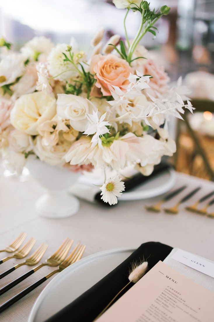 Close-up of delicate peach and white floral centerpiece with gold cutlery on wedding table.