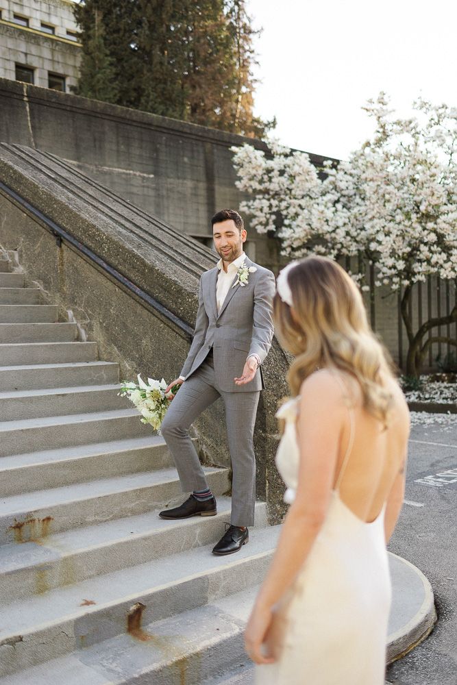 A wedding photo on concrete steps with cherry blossoms and modern architecture.