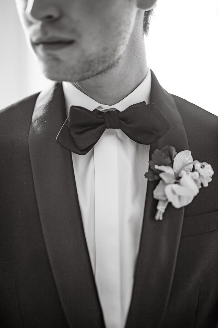 Close-up detail of a black bow tie and boutonniere on a formal tuxedo.