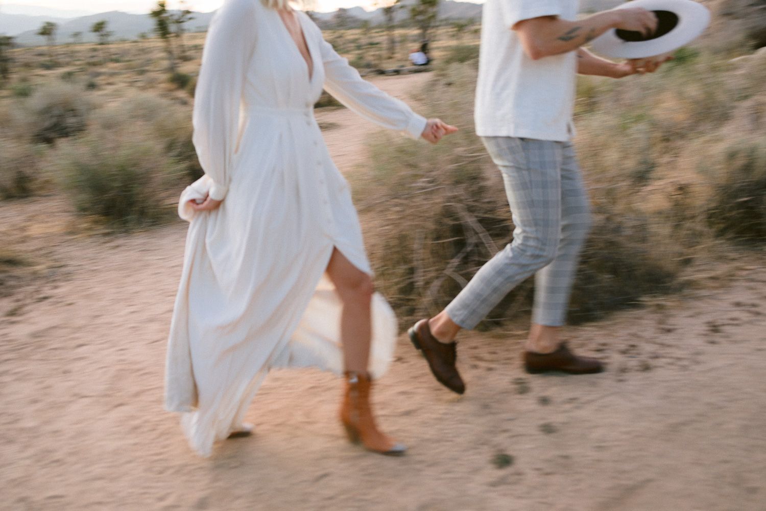 Two people walking on a desert path wearing white and casual attire.