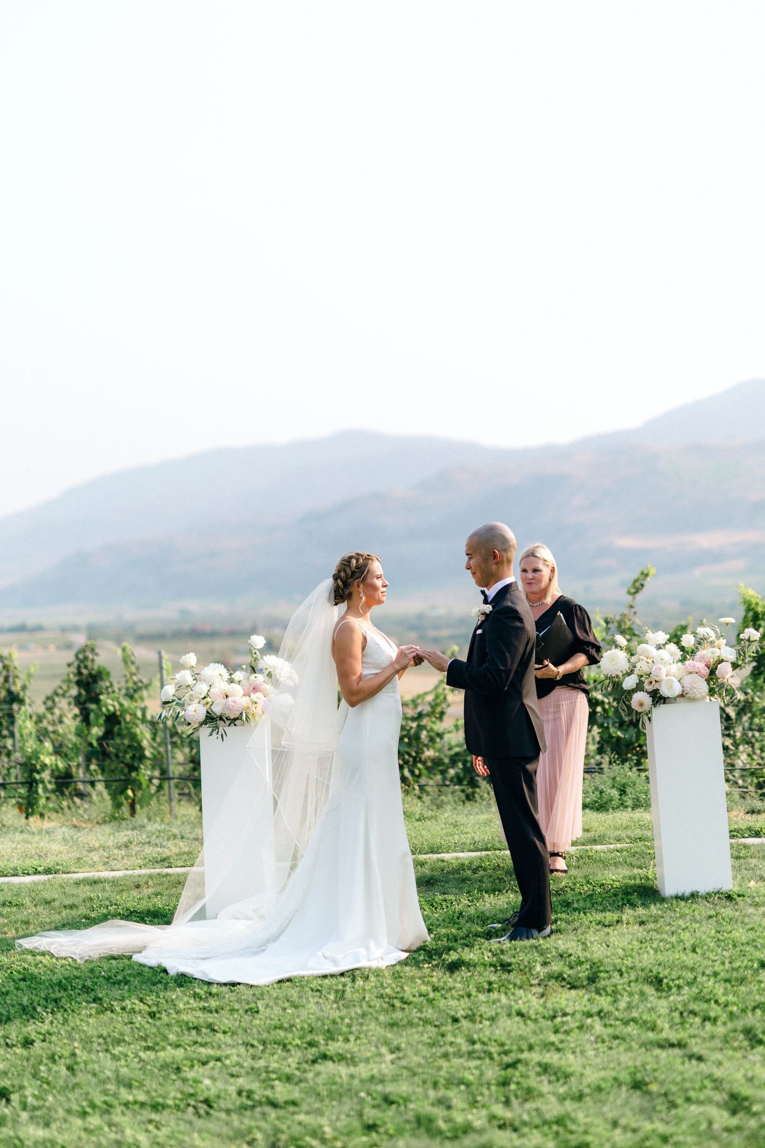 A scenic vineyard wedding ceremony with mountain views and white floral arrangements.