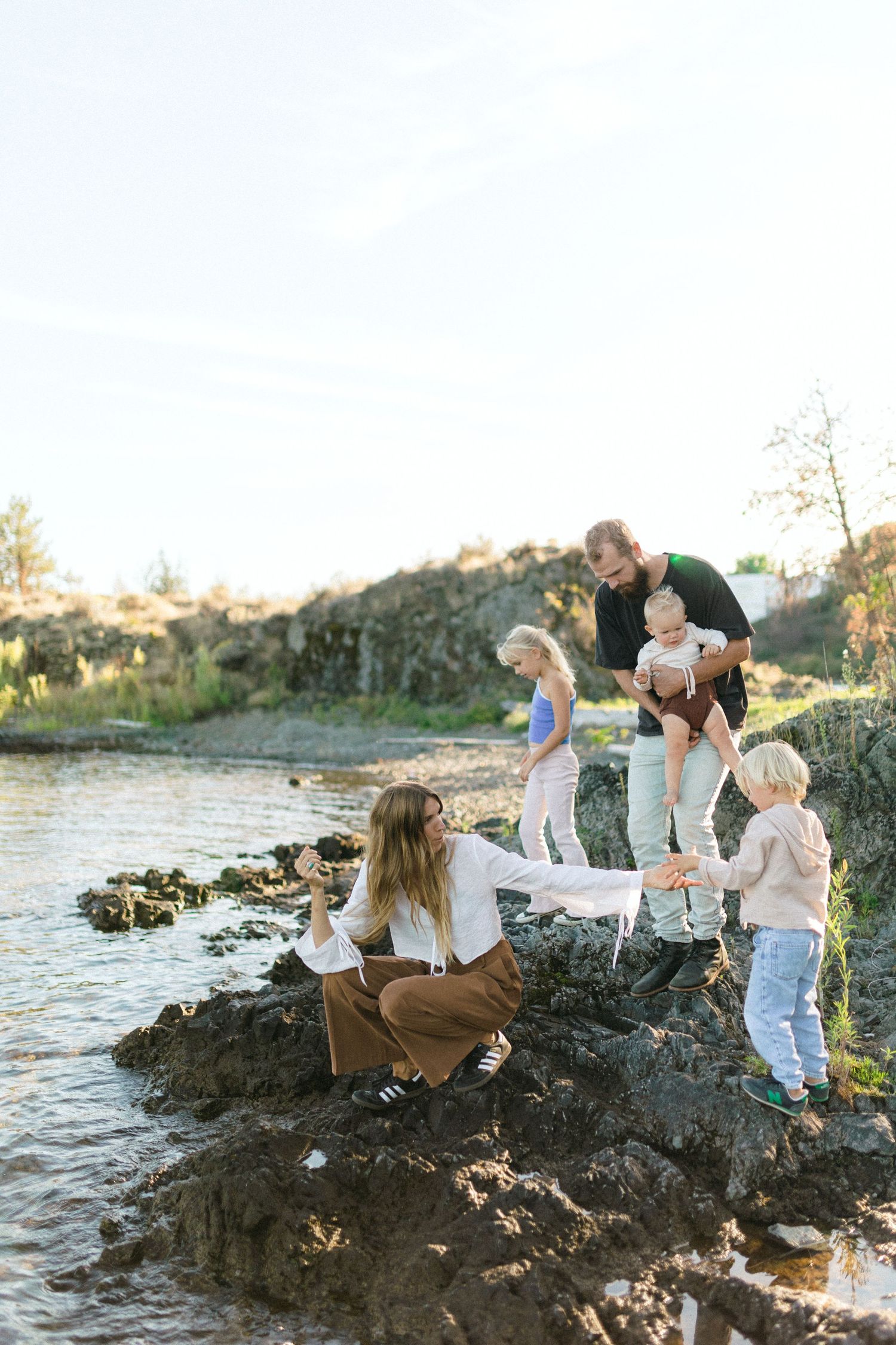 Family enjoying time together exploring rocks by a river on a sunny afternoon at golden hour.