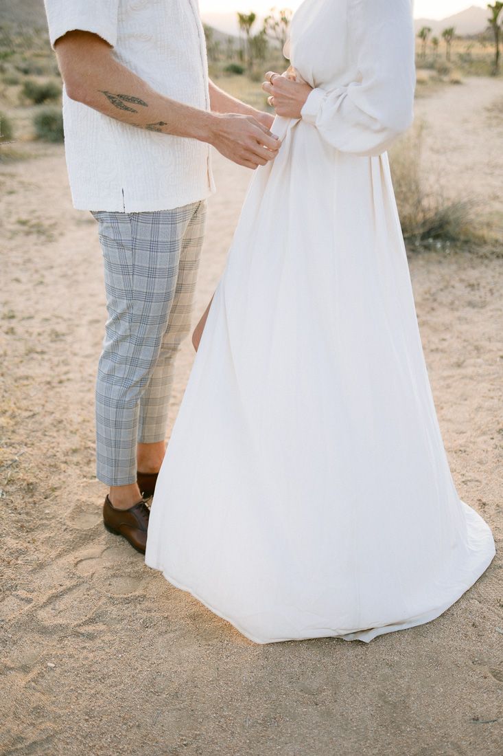 Close-up detail shot of a couple's outfits showing plaid pants and a flowing white dress in a desert setting.