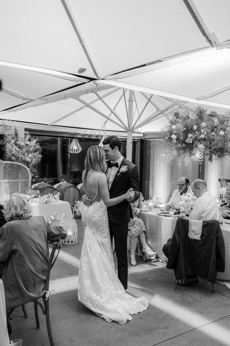 Couple dances beneath white canopy during wedding reception while guests dine at decorated tables.
