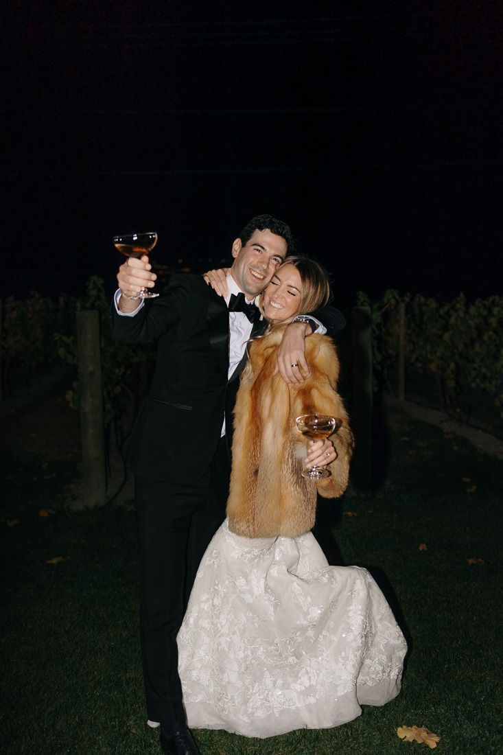 Couple celebrating with wine glasses in a nighttime vineyard setting.